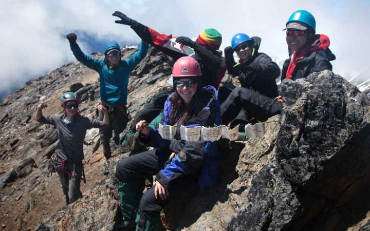 a group of students smile and celebrate reaching the summit of a mountain
